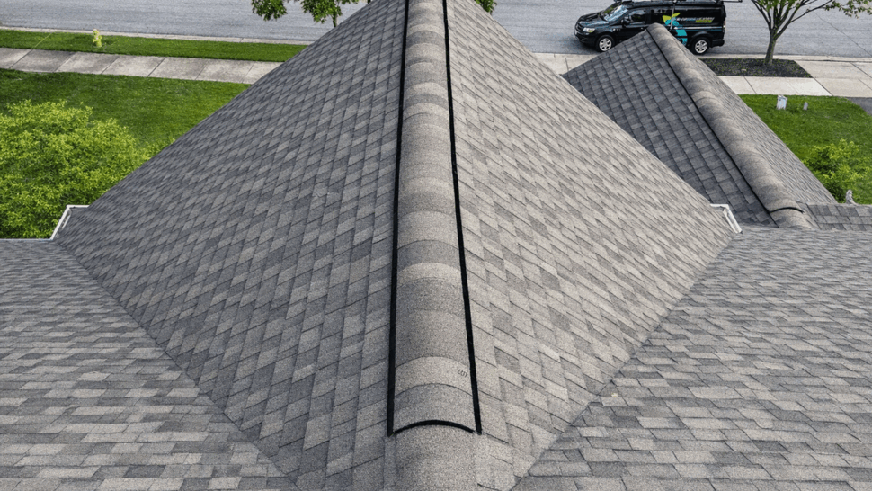 Aerial close-up of shingled roof ridge with vent and Tycos truck visible on the street