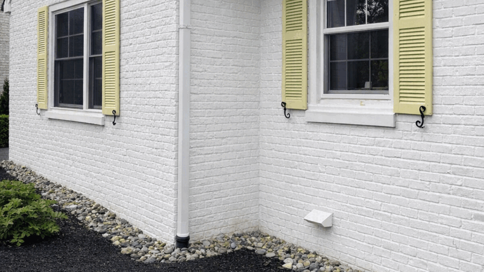 White brick gutter corner | Tycos Roofing And Siding Inc Corner of white brick house with black gutter, downspout, and pale shutters