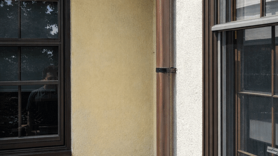Close-up of copper gutter and vertical downspout beside stucco wall and window