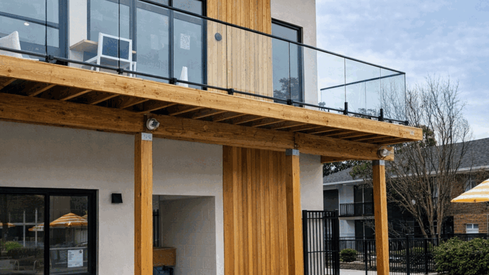 Modern Glass Balcony and Deck | Tycos Roofing And Siding Inc Two-story home with glass balcony, wooden posts and patio chairs.