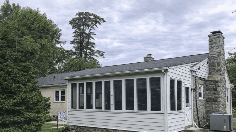Enclosed Sunroom Addition with Windows | Tycos Roofing And Siding Inc Side view of enclosed sunroom with multiple windows next to stone chimney