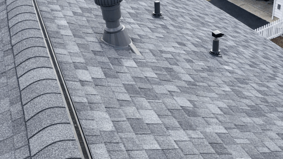 Close-up of gray asphalt shingles with multiple roof vents and ridge vent