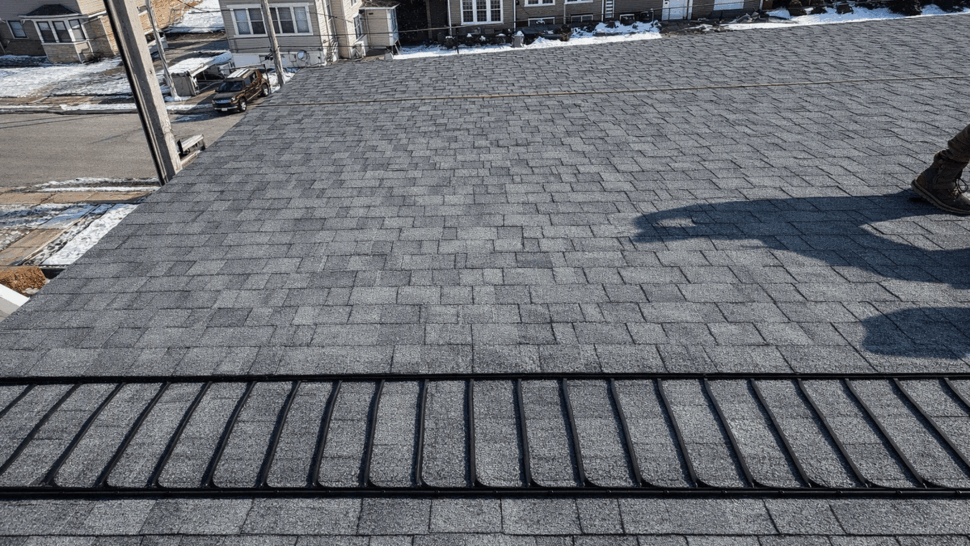 Overhead view of a gray shingle roof with a ridge vent and neighborhood below