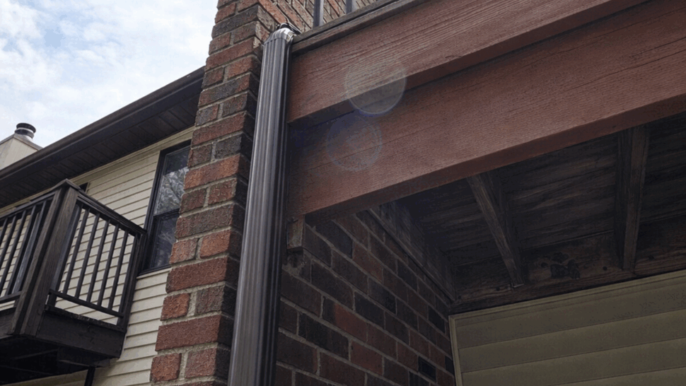 Brick chimney with vertical downspout and balcony railing above.