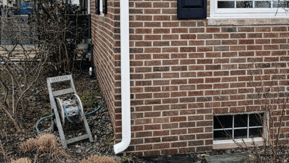 Gutter and downspout on brick home | Tycos Roofing And Siding Inc Close-up of a white downspout and gutter attached to the brick corner of a house