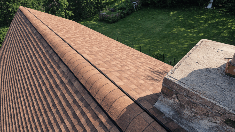 Close-up of shingle ridge and ridge vent | Tycos Roofing And Siding Inc Close-up of a brown shingle roof ridge with ridge vent next to a chimney.