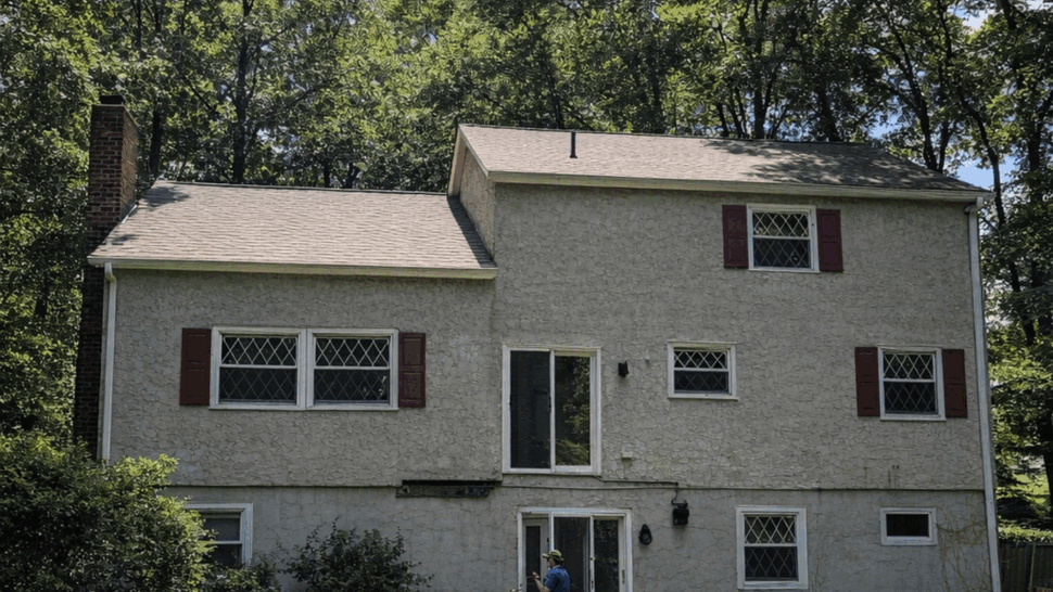Rear of house with a pool, patio chairs, and a worker standing near the patio steps.