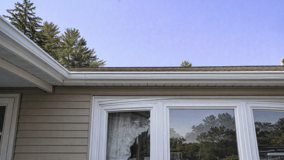 Bay window and roofline with gutter | Tycos Roofing And Siding Inc Bay window beneath a roofline with an attached gutter on a beige sided home