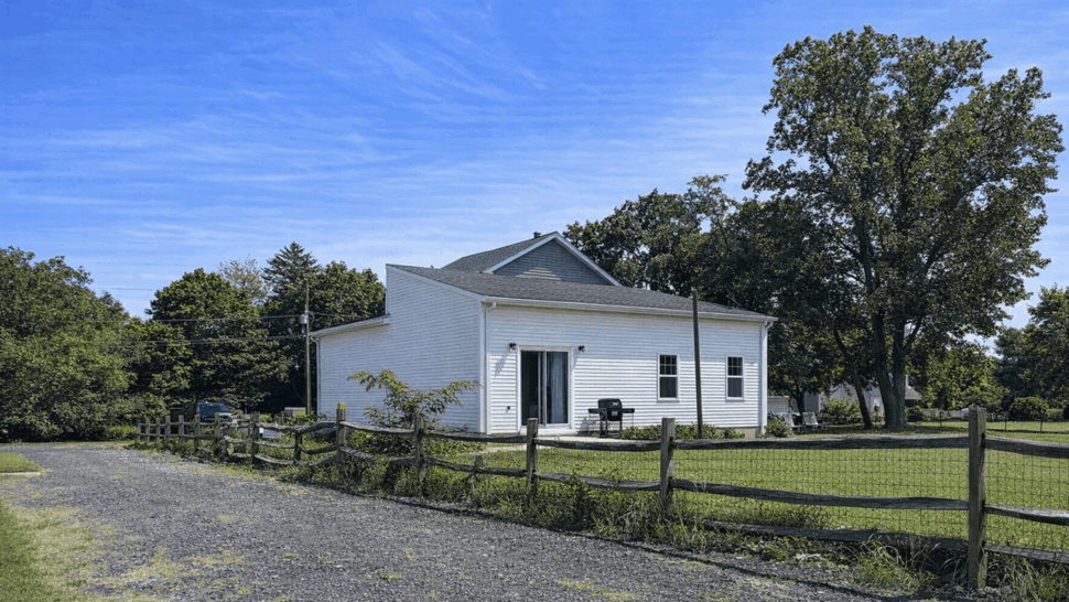 White home siding with split-rail fence | Tycos Roofing And Siding Inc White house exterior with vinyl siding, fenced yard and gravel driveway under blue sky