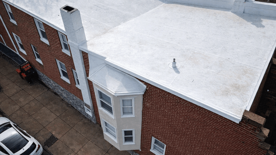 Aerial view of a white flat rooftop with a chimney on a brick building