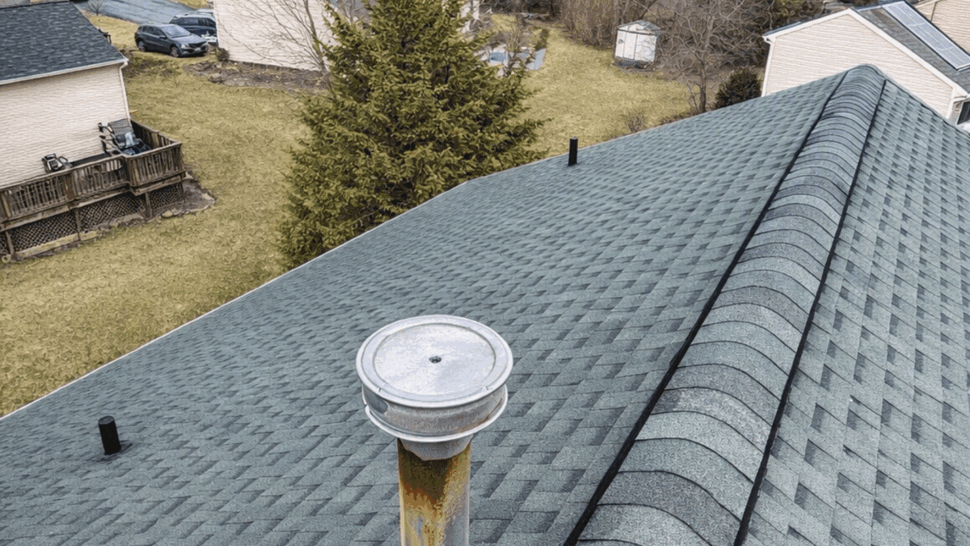 Close-up of green asphalt shingles and a vent pipe on the roof.