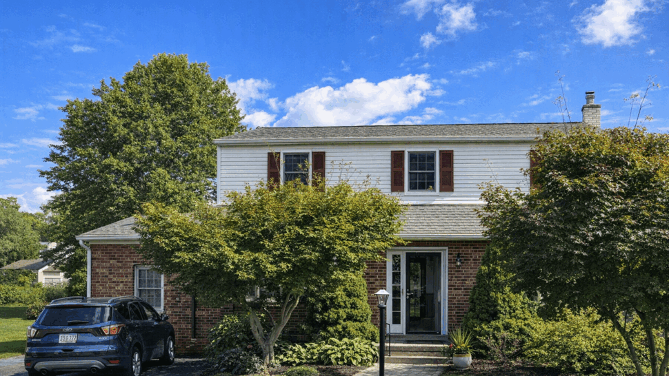 Two-story colonial house front with white siding, brick first floor, landscaping and driveway.
