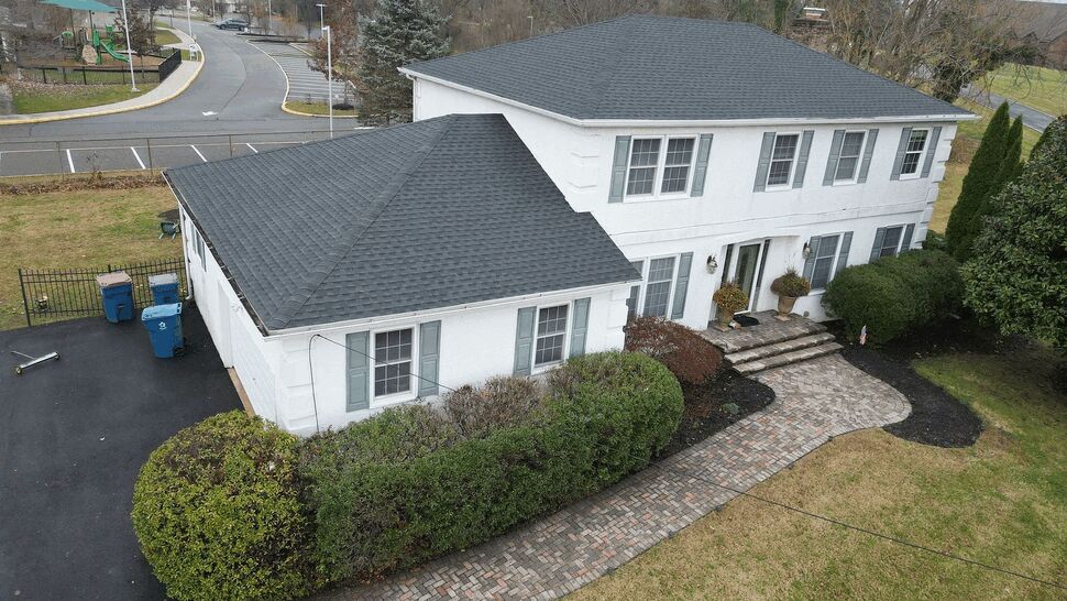 Aerial view of a two-story white home with dark shingled roof and brick walkway.