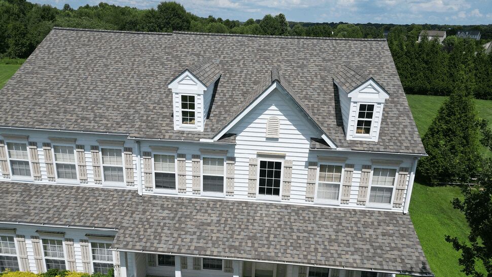 Aerial view of white house roof with dormers and gray asphalt shingles.