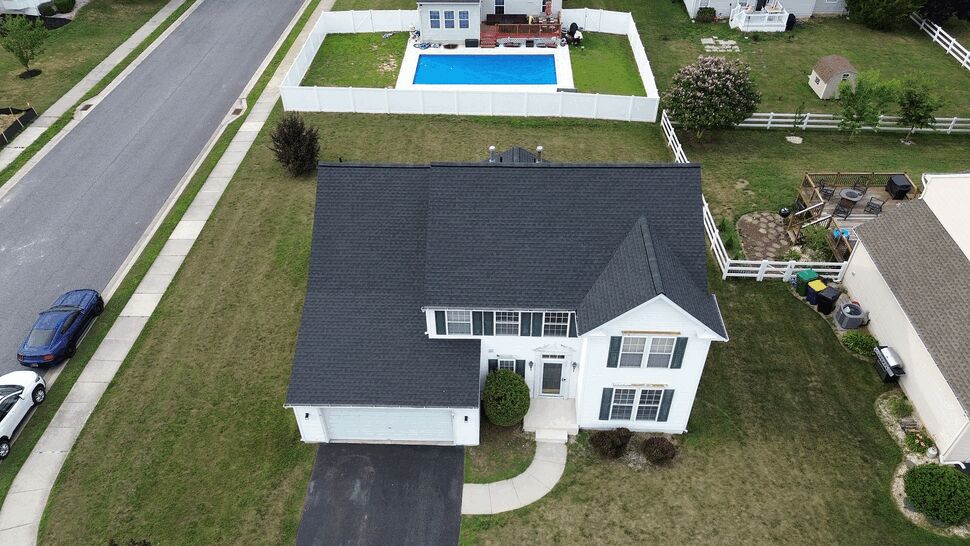 Aerial view of a two-story home with dark shingle roof and driveway.