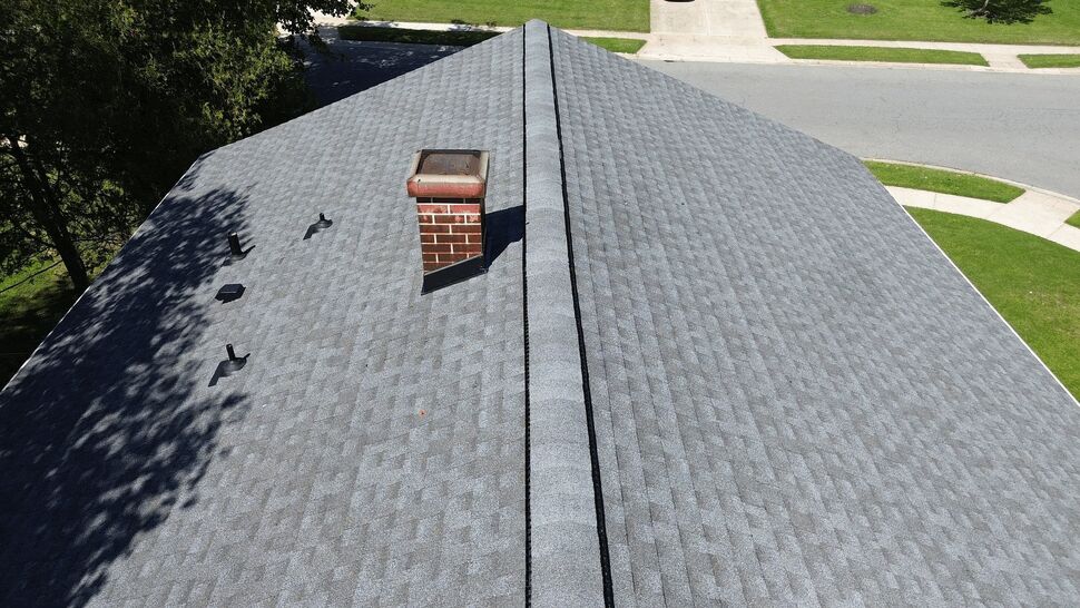 Aerial roof ridge with chimney | Tycos Roofing And Siding Inc Aerial view of gray asphalt shingle roof ridge with chimney and ridge vent.