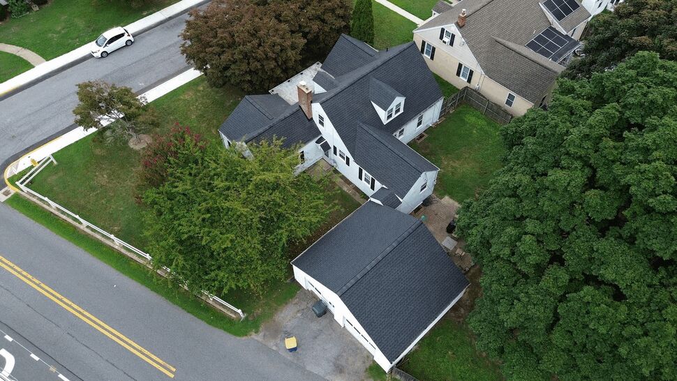 Aerial view of a house and detached garage roofs with surrounding trees and street.