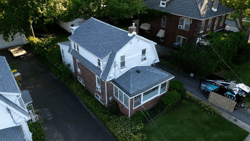 Aerial view of a residential grey shingle roof with a Tycos dumpster parked next to the driveway.