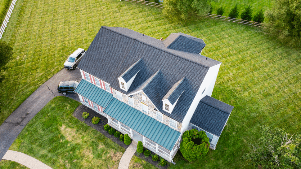 Angled aerial view of house roof, dormers and surrounding yard