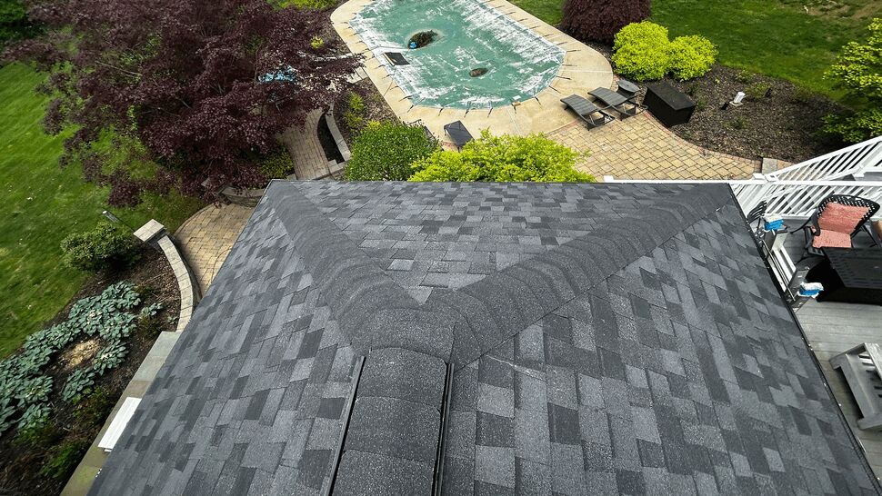 Aerial perspective of dark shingle roof above backyard pool and patio
