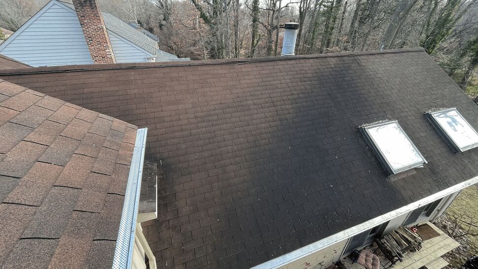 Aerial view of a shingled roof with two skylights, gutter and visible staining