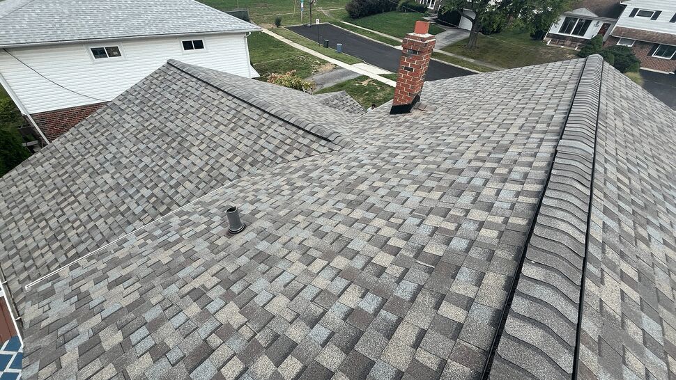 Aerial view of grey composite shingle roof showing ridge vent and nearby chimney.