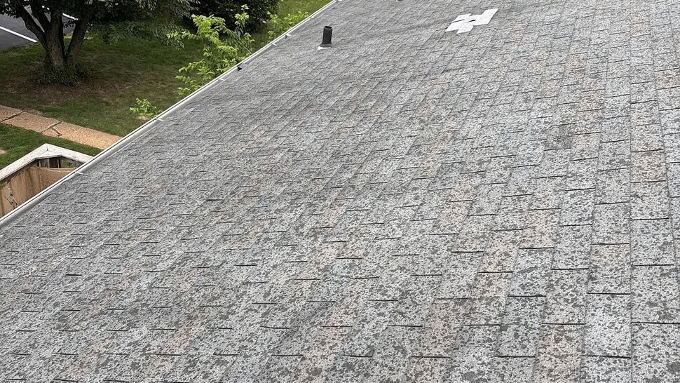 Aerial view of shingled roof with vents and a patched area showing granule loss.