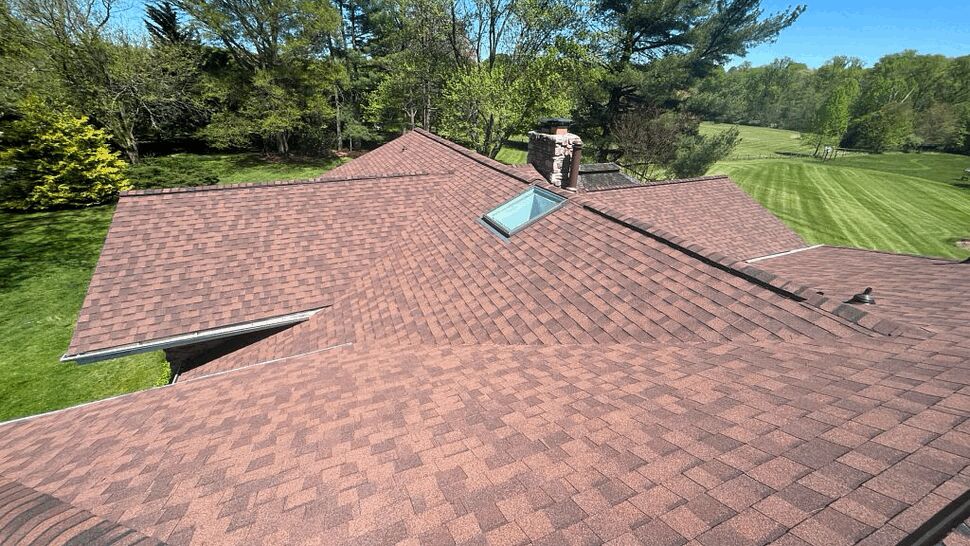 Aerial view of newly shingled roof with skylight and surrounding trees