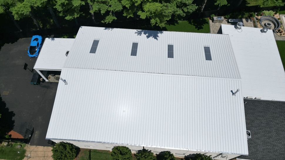 Aerial view of a white metal commercial roof with skylights and surrounding trees.