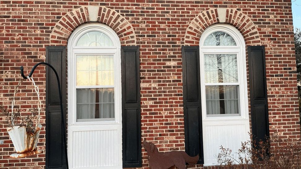 Pair of arched windows with black shutters in a brick facade