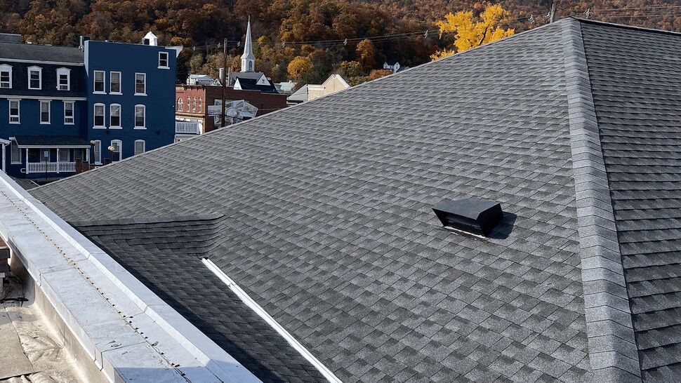 High-angle view of dark gray asphalt shingle roof and rooftop vent