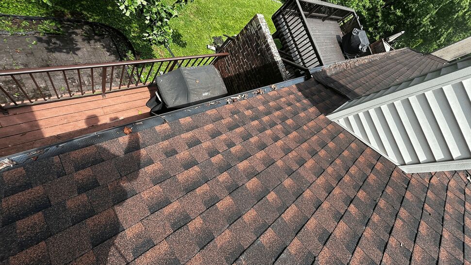 Top-down view of asphalt shingle roof with deck and railings below.