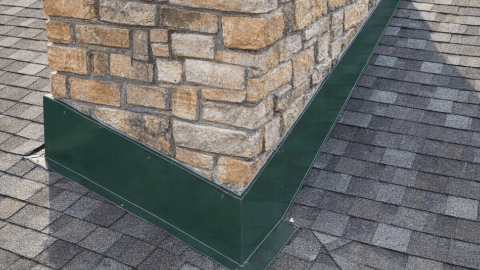 Chimney flashing repair on shingle roof | Tycos Roofing And Siding Inc Stone chimney base with fresh green metal flashing seated on asphalt shingles.