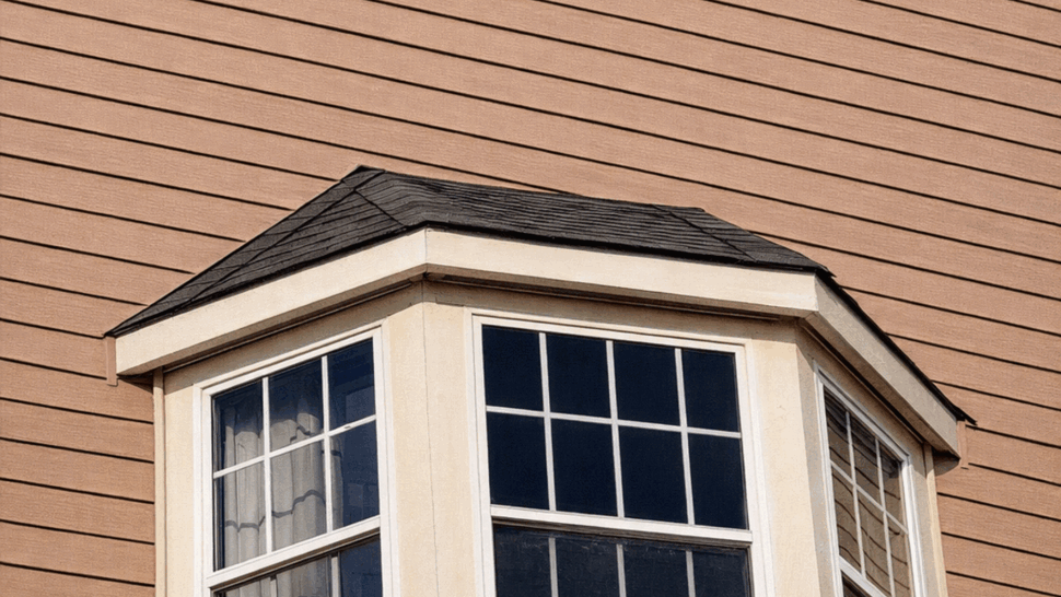 Exterior Bay Window Detail | Tycos Roofing And Siding Inc Three-panel exterior bay window with a small overhanging roof against tan siding.
