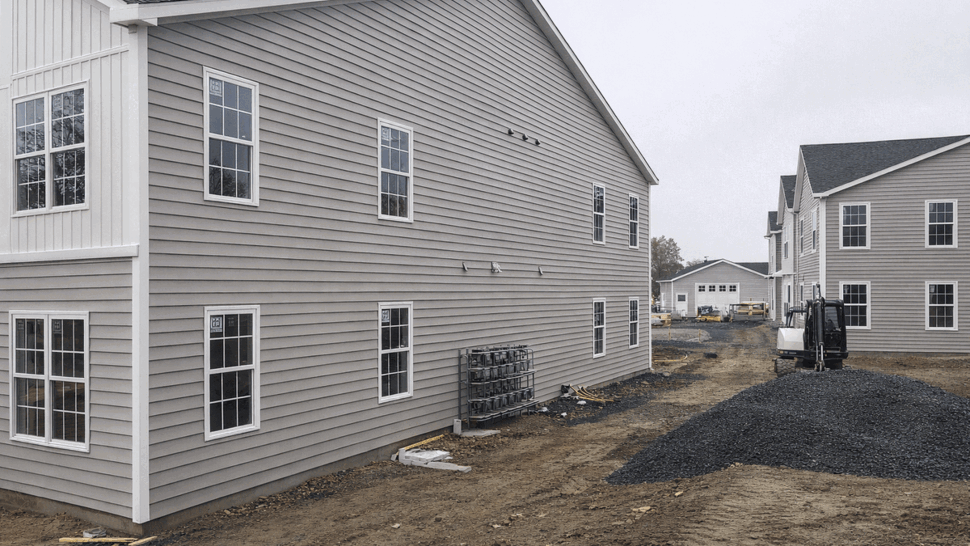 Side view of building with gray siding, multiple windows and construction materials
