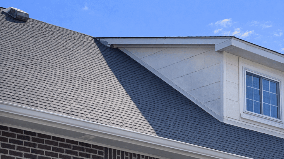 Close-up of dormer and roof showing shingles and damaged fascia near the eave.