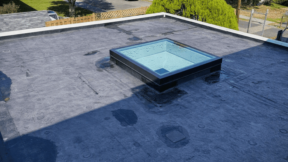 Flat membrane roof with skylight and visible water patches