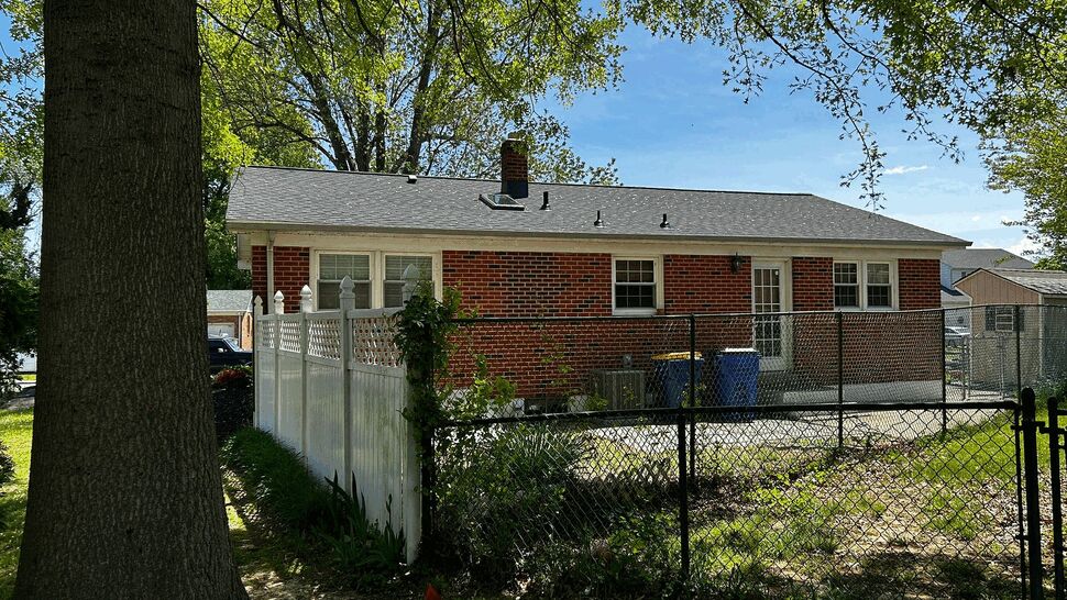 Rear view of brick house with white gable siding, fenced backyard and skylight.