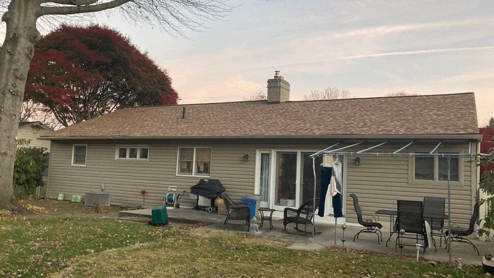 Rear view of house with brown roof, beige siding, sliding door and patio furniture