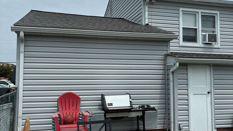 Rear shingle roof and vinyl siding above a backyard patio area