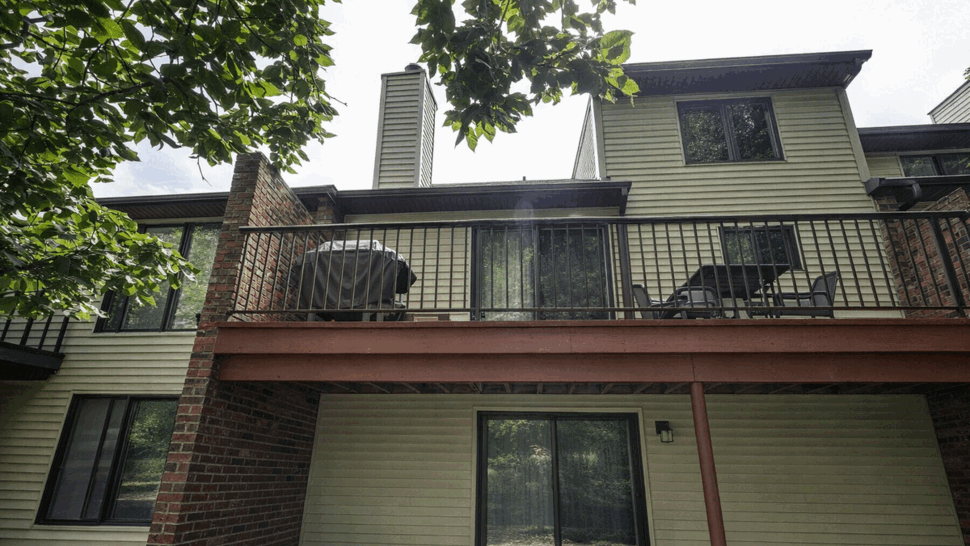 Rear two-level deck with metal railing, sliding door and brick chimney.
