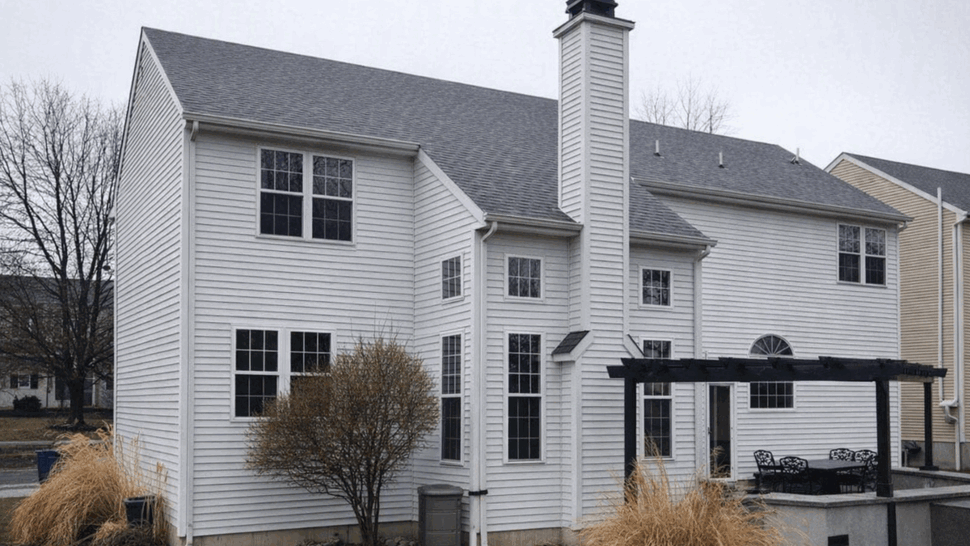 Rear view of white vinyl siding house with chimney, gutters and pergola over patio