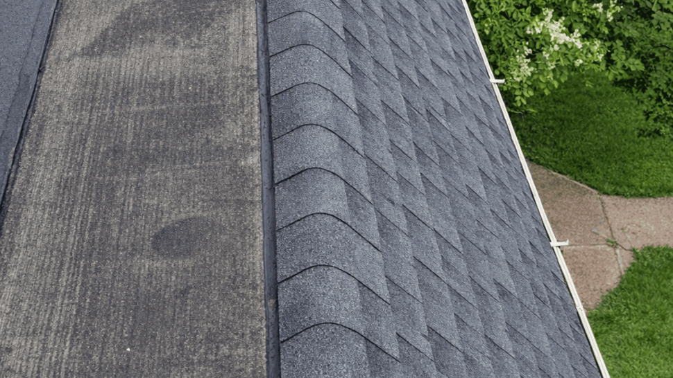 Aerial view of gray asphalt shingle roof and adjacent flat ledge with white gutter.