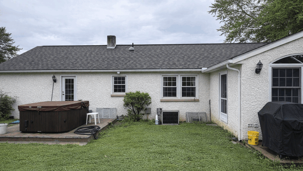 Backyard roof view over stucco home | Tycos Roofing And Siding Inc Rear view of stucco house with hot tub on a small deck and shingled roof above