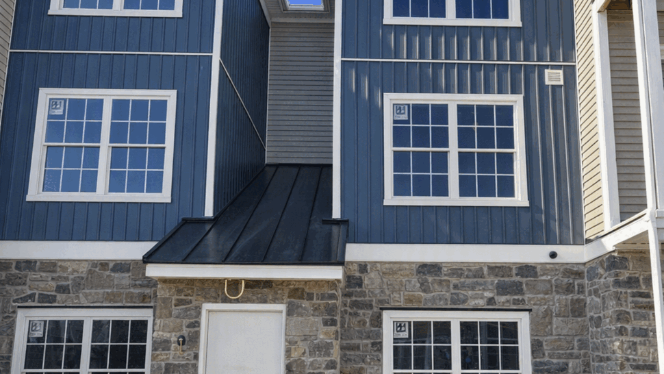 Blue vertical siding panels with white-trim windows beneath a clear sky