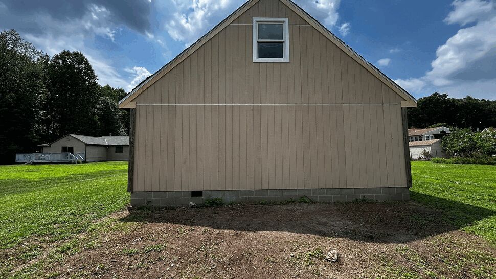 Beige gable end with small upper window and vertical siding under a partly cloudy sky