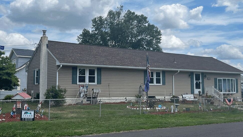 Front view of a beige single-story home with siding, gutters, and yard decor.