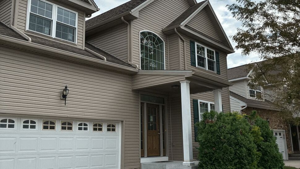 Two-story beige house with white garage door, vinyl siding and a front porch.