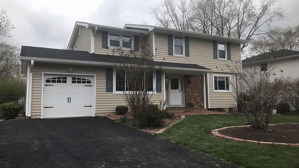 Front view of two-story beige home with garage, black roof shingles and white trim.