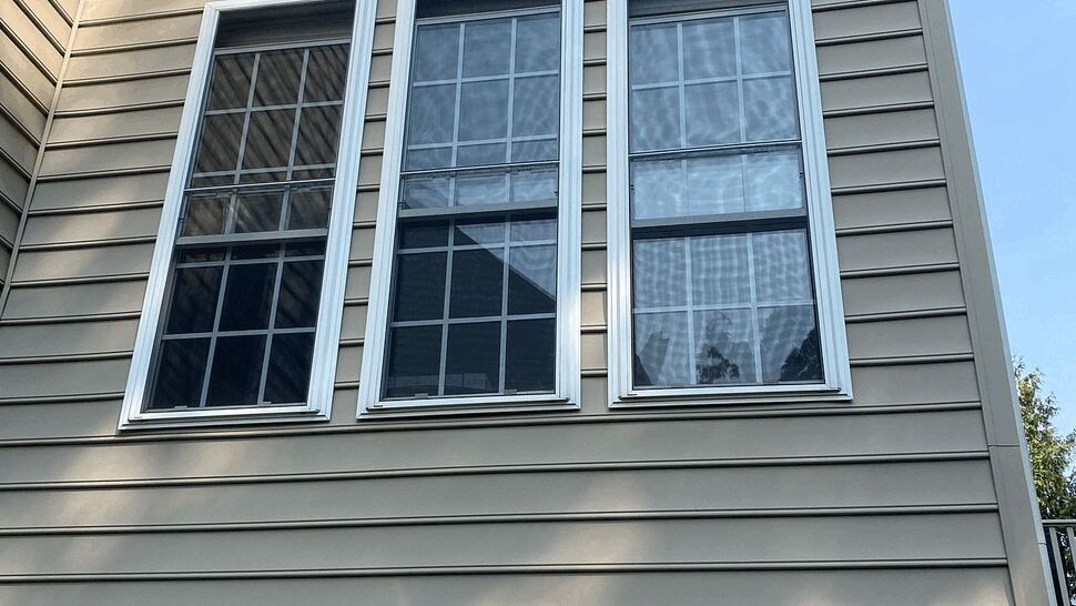 Close-up of beige vinyl siding with three tall white-trimmed windows.
